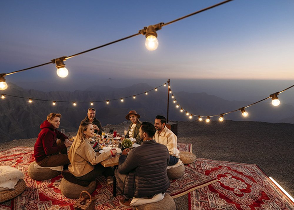 A group dining outdoors under string lights on Jebel Jais at dusk